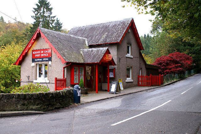 A red-roofed building labeled 'Bridge of Caled Post Office' with a signboard and a red fence.
