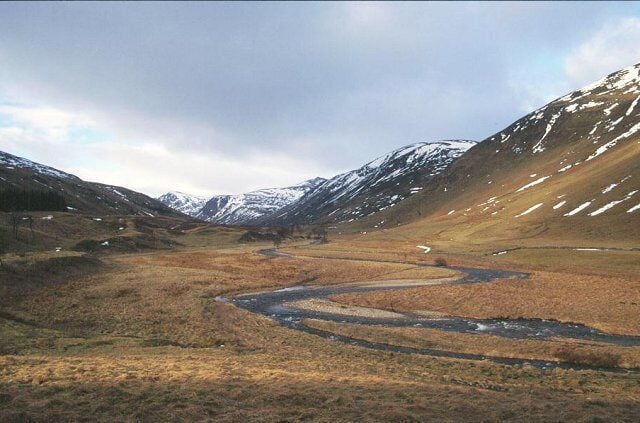 A winding river in a mountainous landscape with snow-capped peaks and sparse vegetation.