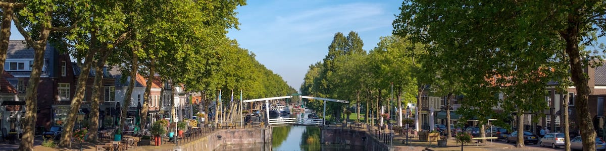 A canal with a bridge, lined with trees and buildings.