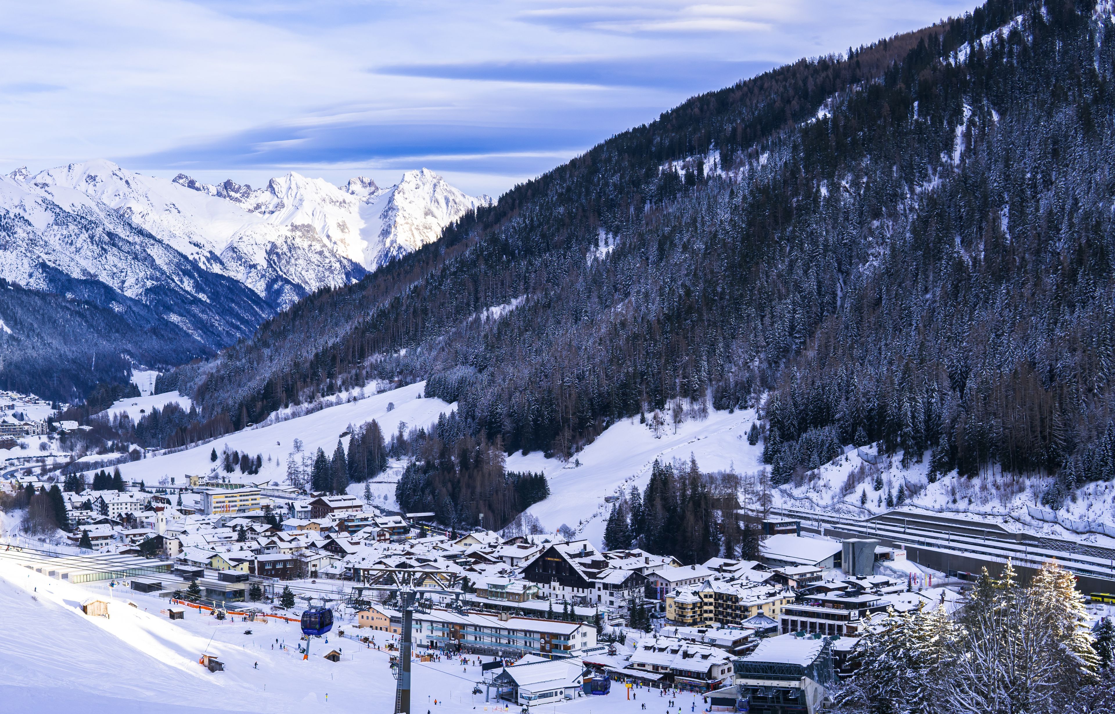 A snow-covered mountain town with ski slopes, buildings, and a forested mountain backdrop.