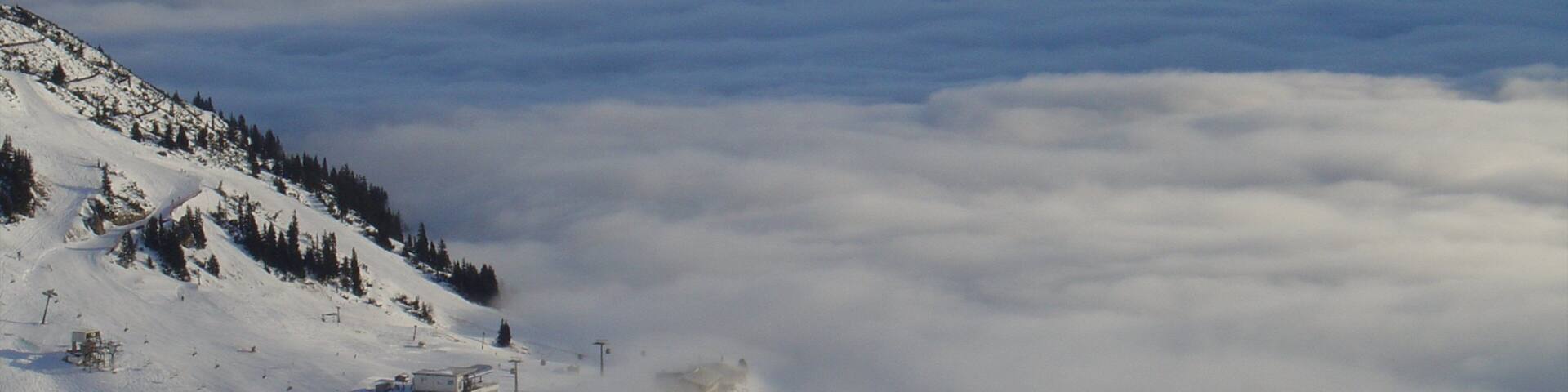 A snow-covered mountain range with a valley of clouds below.