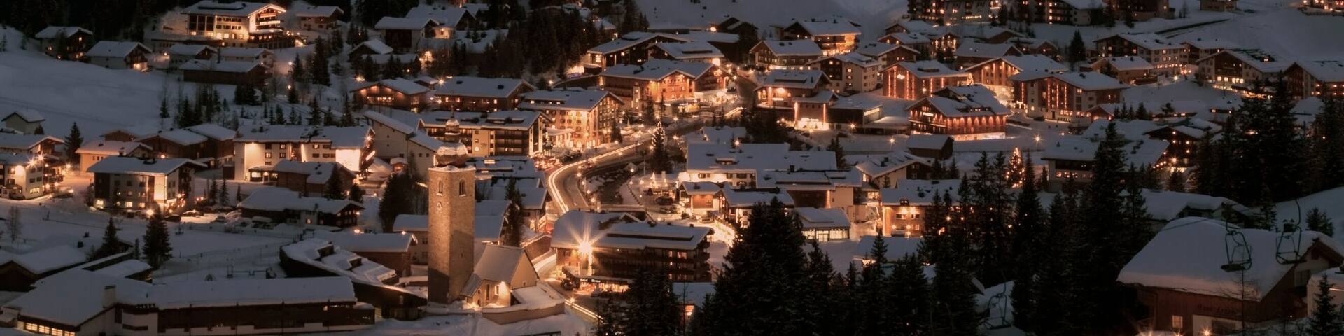 A snow-covered mountain range at dusk with a town in the foreground.
