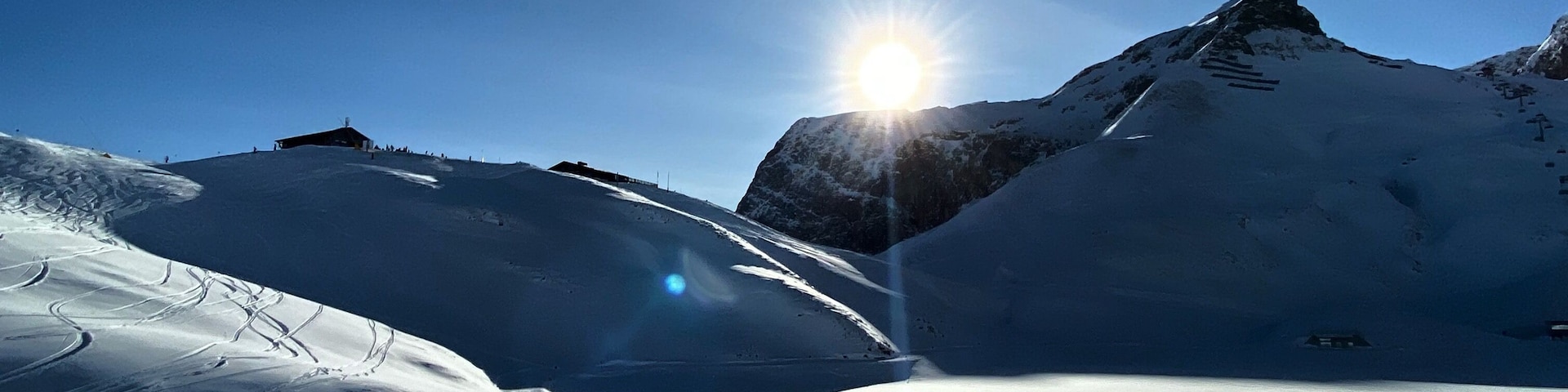 A snowy mountain landscape with a clear sky and the sun shining through.