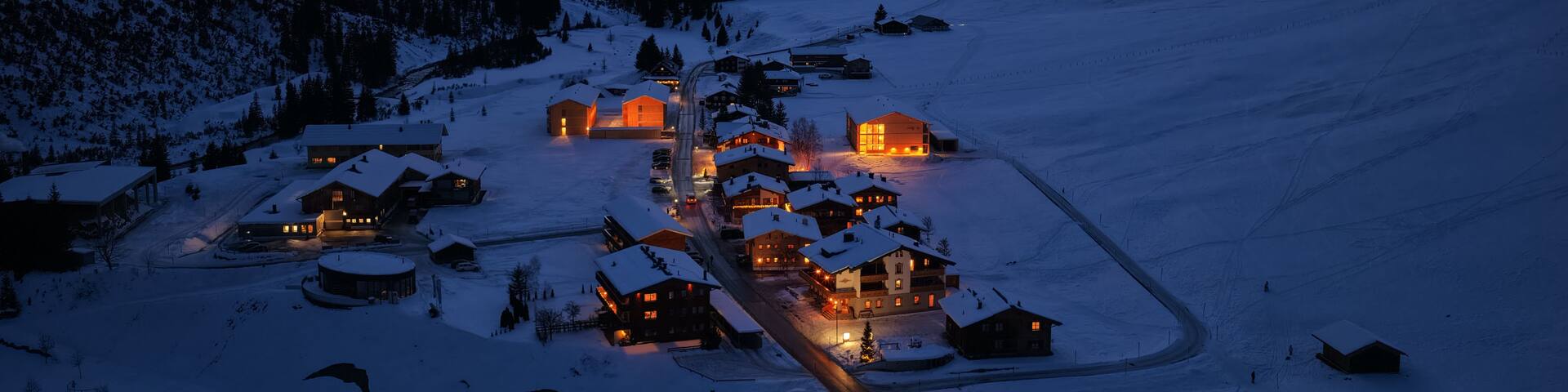 Aerial view of the snow-covered village of Lech am Arlberg with glowing lights from houses nestled among alpine peaks at twilight Lech am Arlberg, Vorarlberg, Austria.