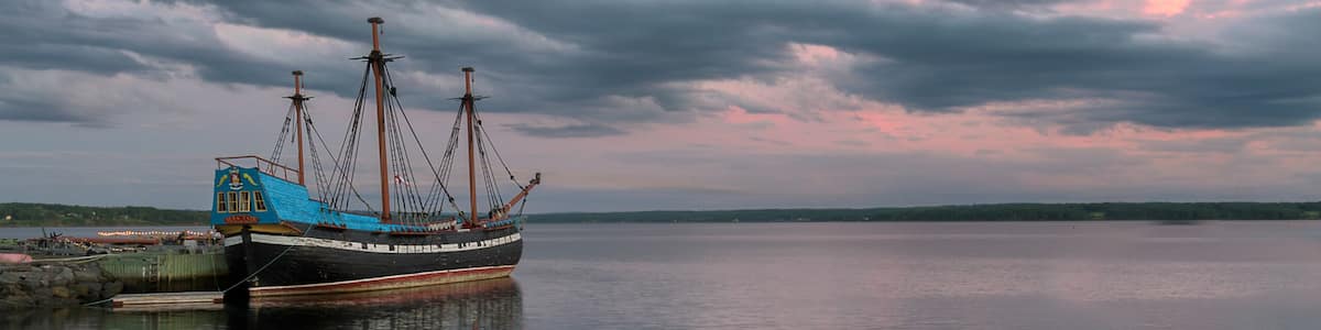 A calm body of water with a ship docked on the left, under a cloudy sky.