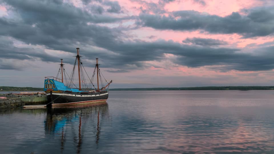 A calm body of water with a ship docked on the left, under a cloudy sky.
