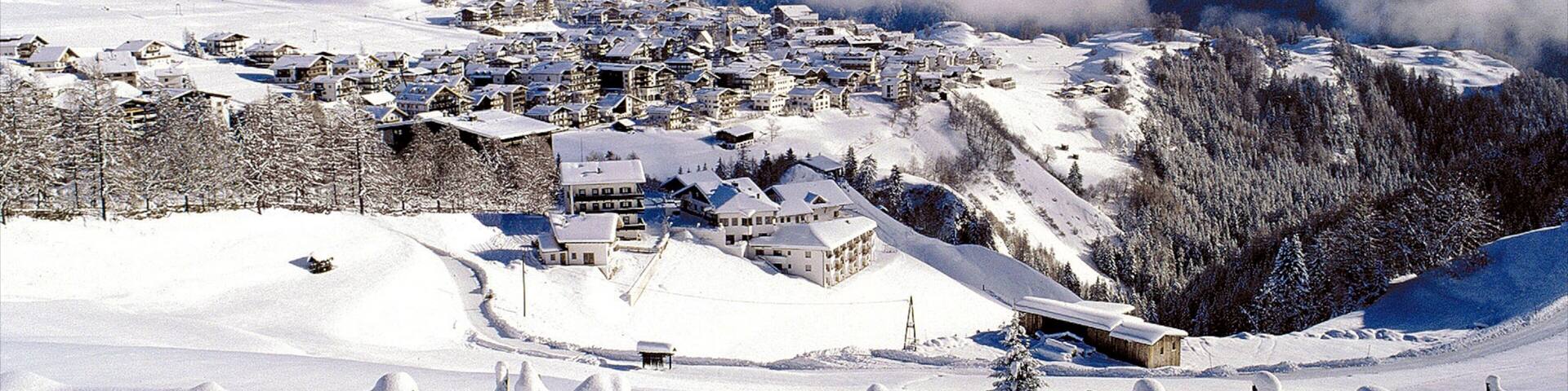 A snow-covered village with houses and a mountain backdrop.