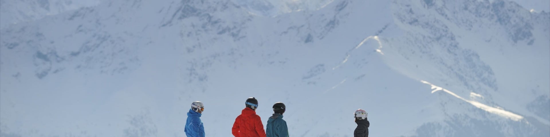Four skiers on a snowy mountain with a backdrop of snow-covered peaks.