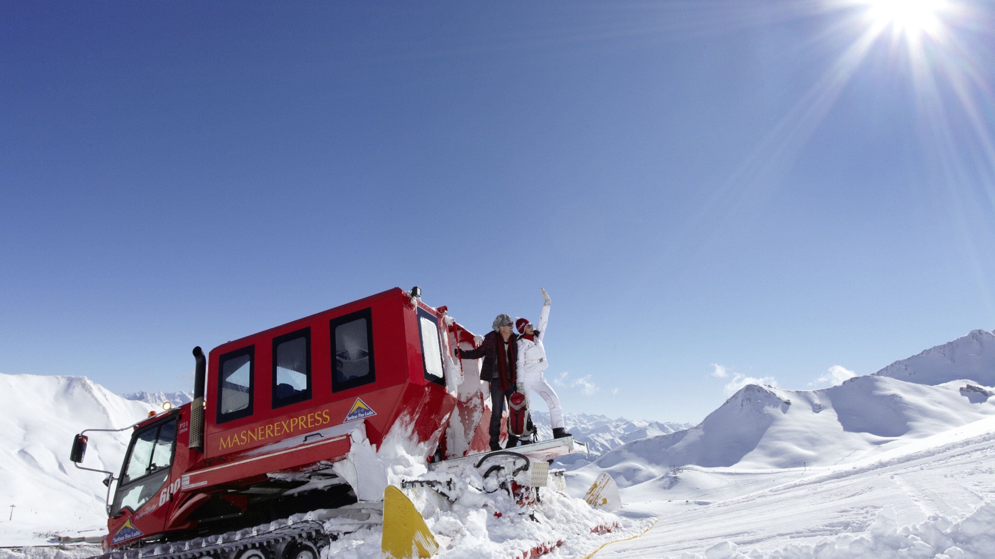 A red Masnerexpress vehicle on a snowy mountain with people celebrating.