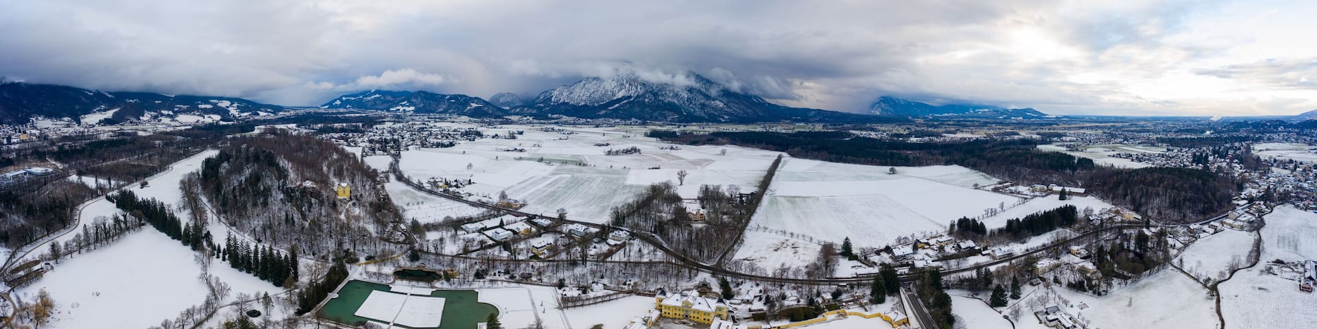 Panoramic aerial view of Salzburg outskirts snowy villages during sunset hour with clouds after snow storm in winter