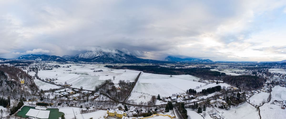A panoramic view of a snow-covered landscape with mountains in the background, a town in the foreground, and a railway track.