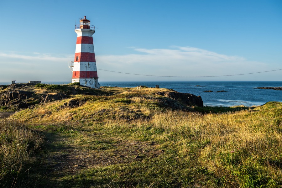 Red-and-white striped lighthouse on the rocky coast of Brier Island, overlooking the Atlantic Ocean under a clear blue sky