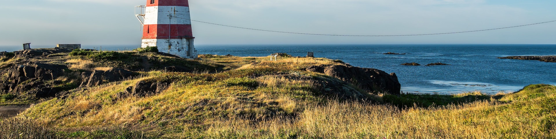 Ein roter und weißer Leuchtturm auf einer grasbewachsenen Klippe mit Blick auf den Ozean.