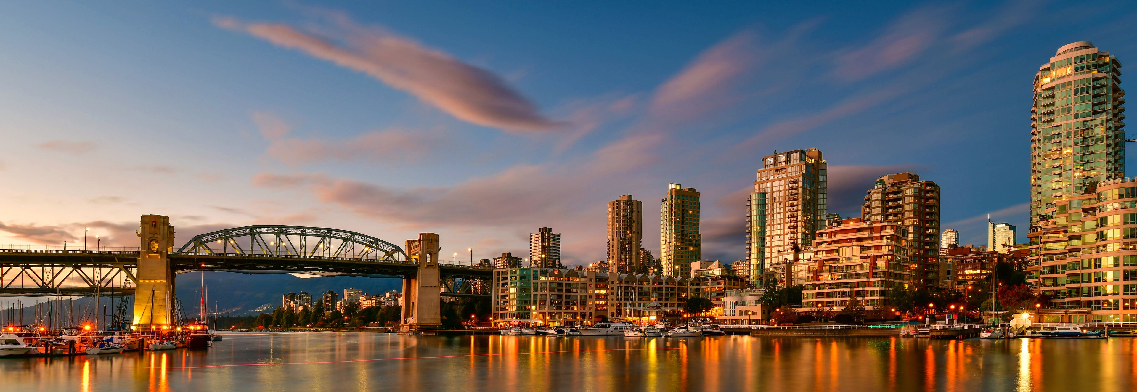 A city skyline with a prominent bridge, high-rise buildings, and a marina with boats.