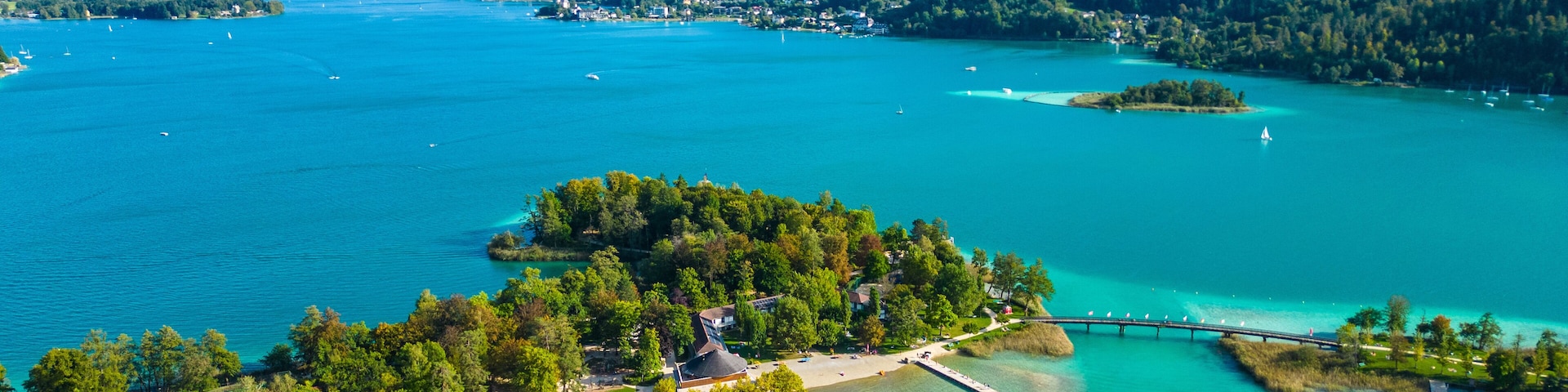 Aerial view of Portschach am Worthersee, Austria, with turquoise lake waters, boats, piers and alpine scenery. Popular summer holiday destination for relaxation, wellness and tourism