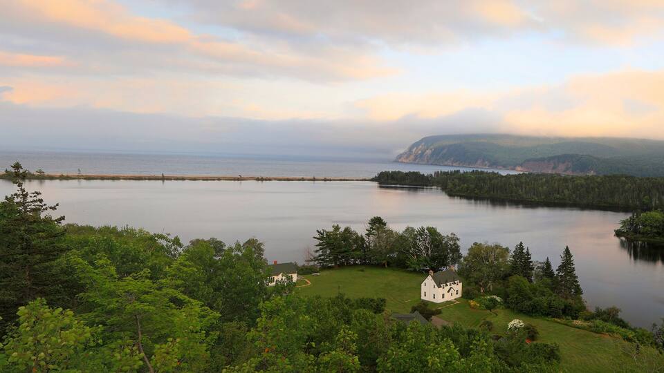 A serene lake surrounded by lush greenery and a white house in the foreground.