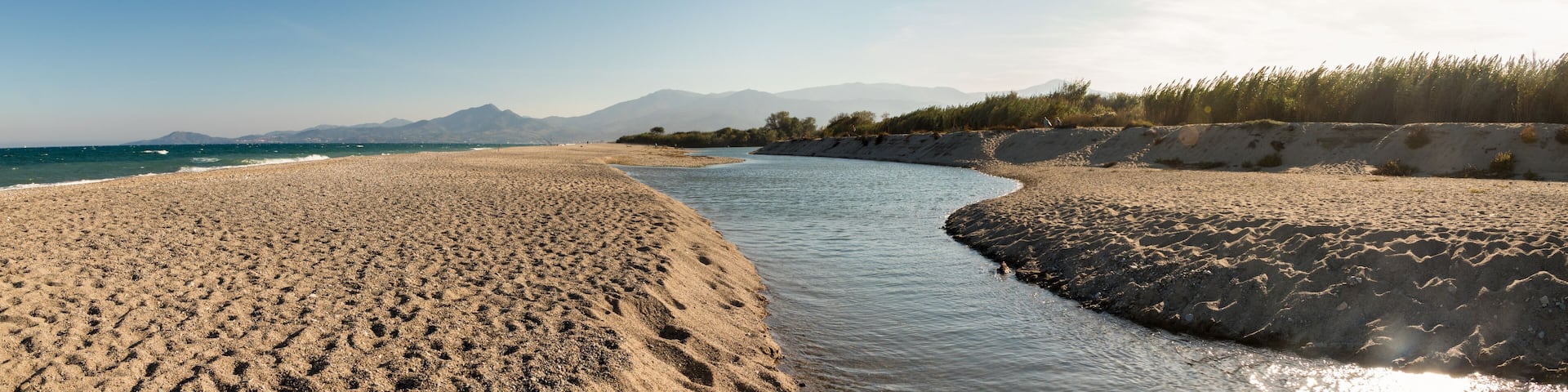 A river flowing through a sandy landscape with mountains in the background.