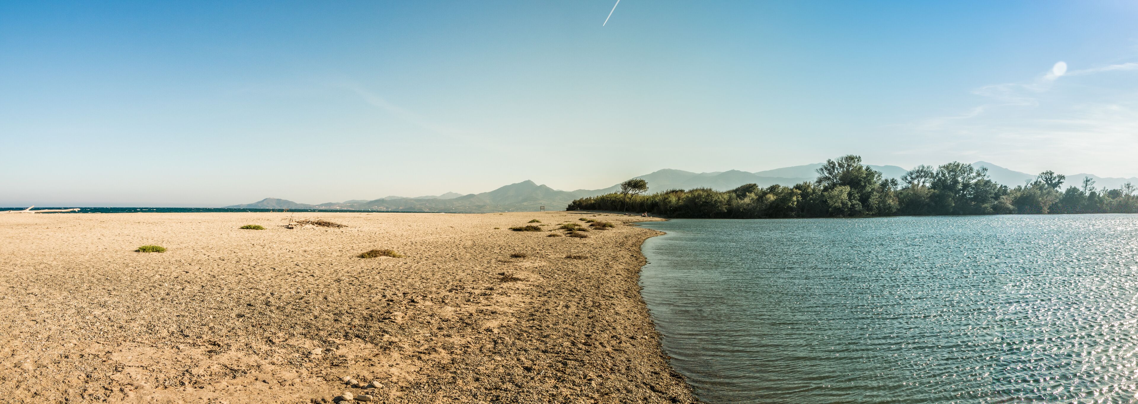 A beach with a sandy shore, calm water, and distant mountains.