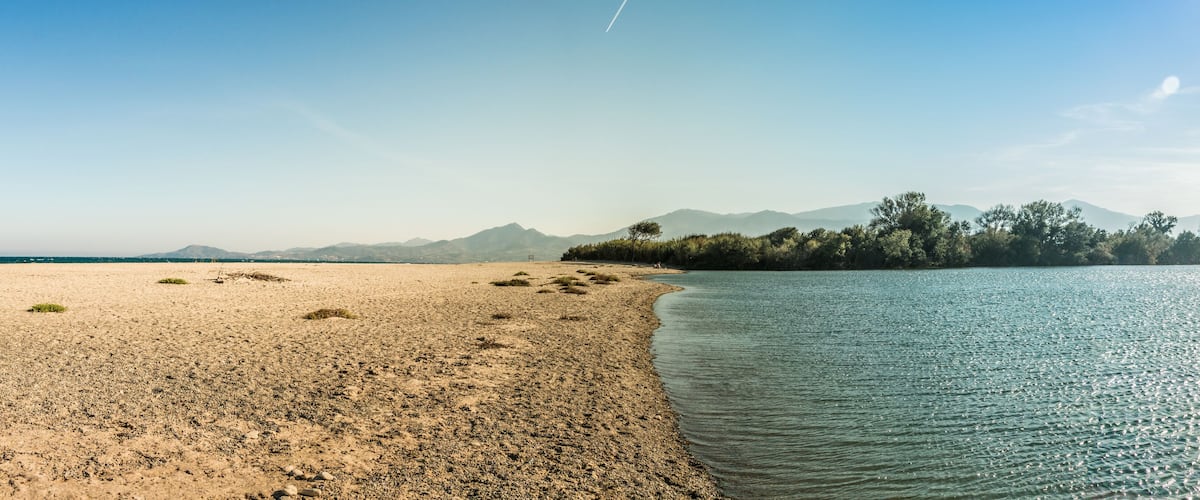 A beach with a sandy shore, calm water, and distant mountains.