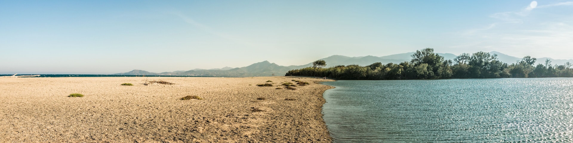 A beach with a sandy shore, calm water, and distant mountains.