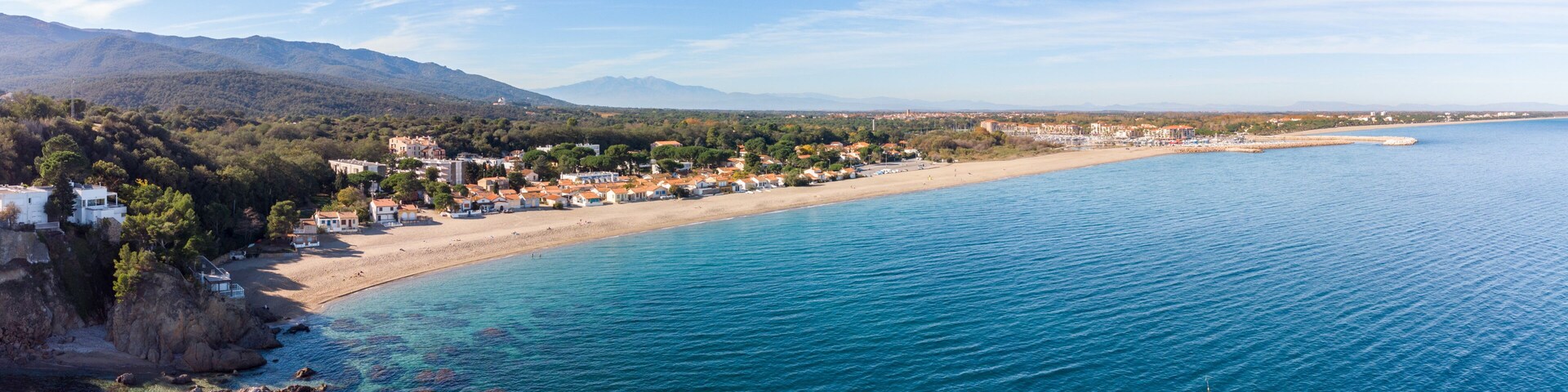 Un pueblo costero con playa, mar azul cristalino y montañas al fondo.