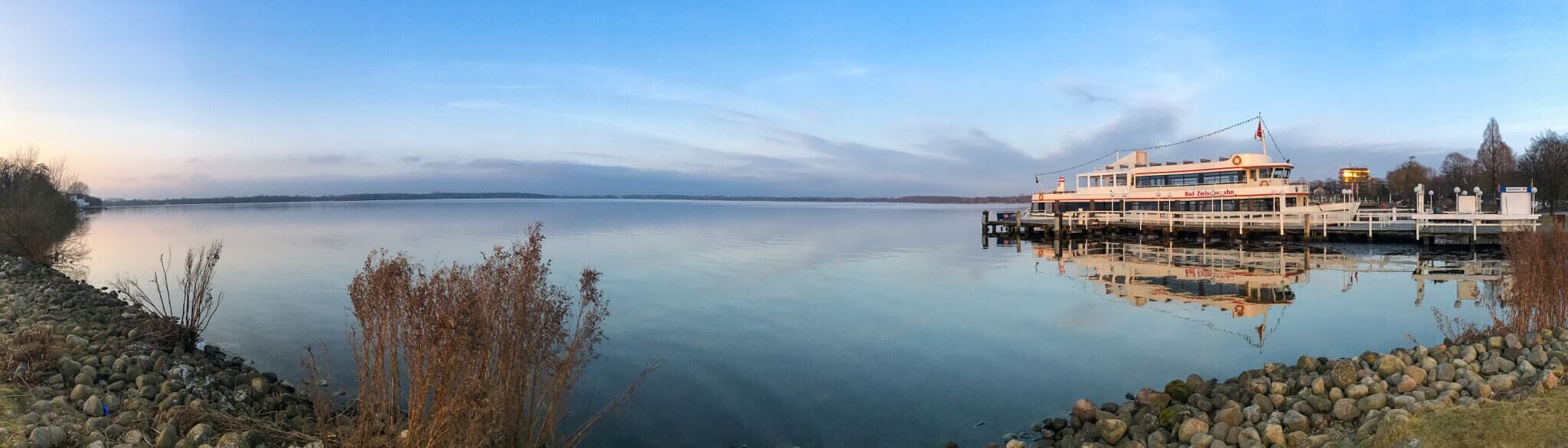 A calm lake with a docked boat and rocky shoreline.