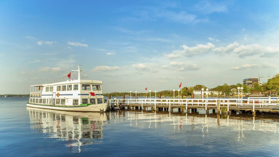 A riverboat docked at a pier with a cityscape in the background.