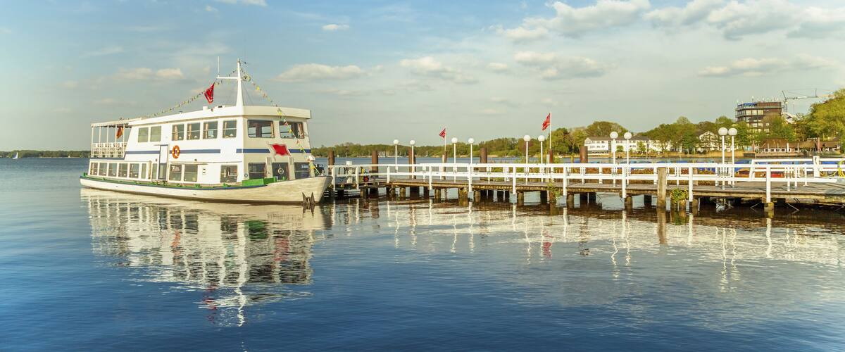 A riverboat docked at a pier with a cityscape in the background.