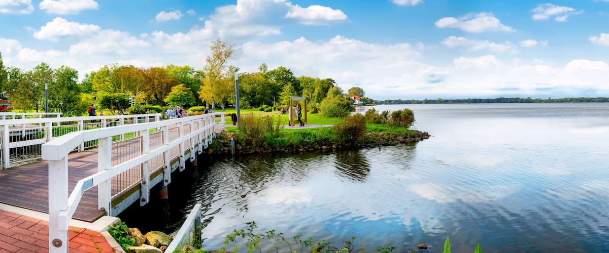 A white bridge over calm water, surrounded by lush greenery and a clear sky.