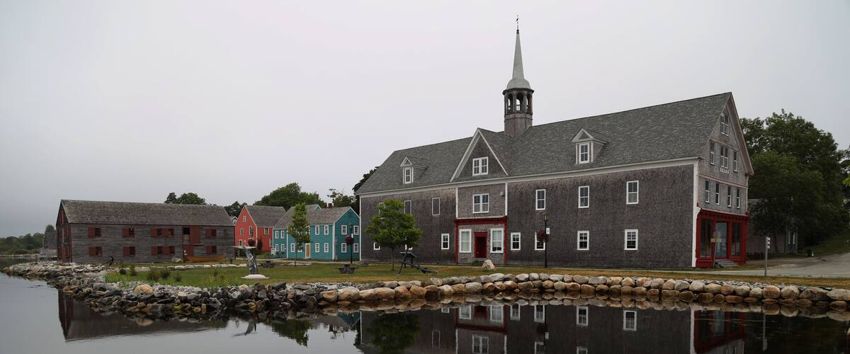 A historic building with a steeple, a stone wall, and a calm body of water reflecting the structure.