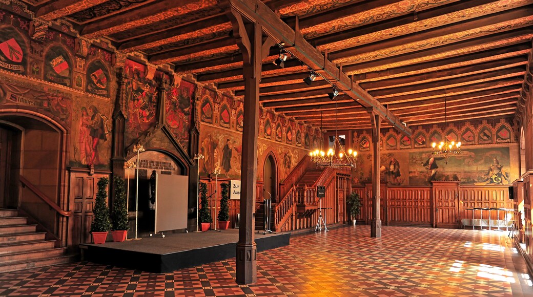 An ornate hall with intricate ceiling designs, a checkered floor, and a grand staircase.