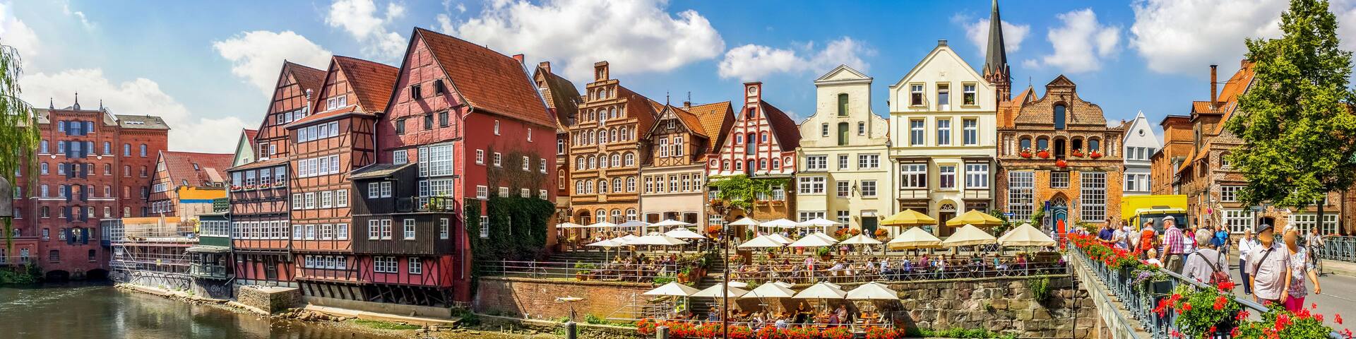 A riverside town with historic buildings, a boat docked at the pier, and outdoor seating at a café.