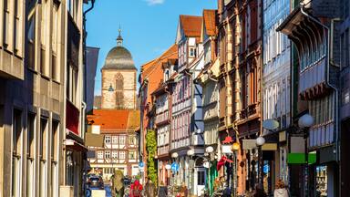 A historic European street with traditional half-timbered buildings, a church with a dome, and a clear blue sky.