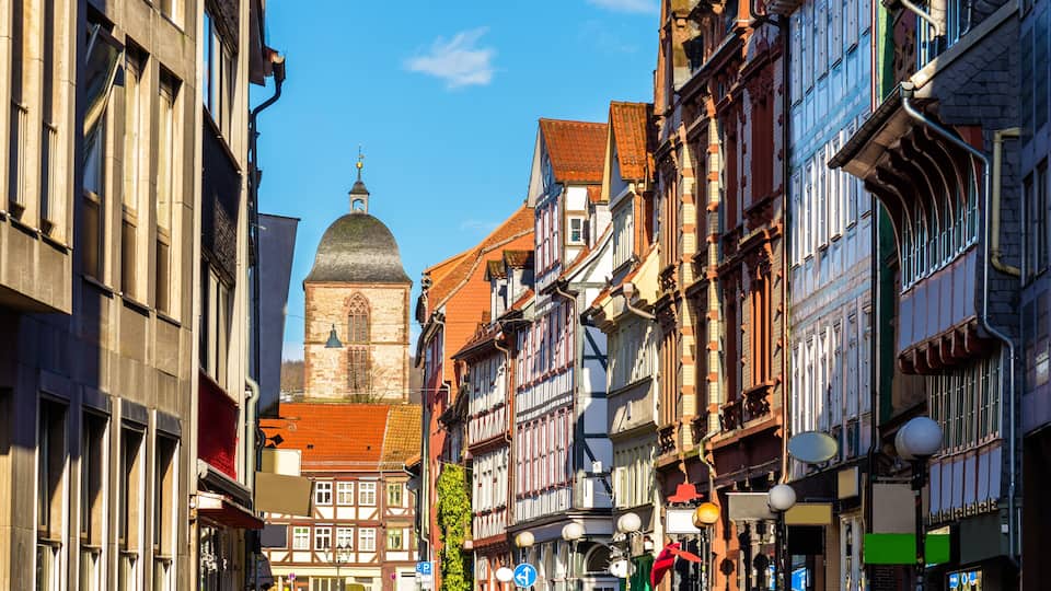 A historic European street with traditional half-timbered buildings, a church with a dome, and a clear blue sky.