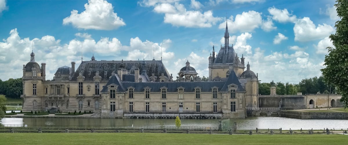 A grand historic building with a large courtyard, a moat, and a river.