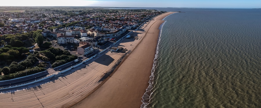 Vista aérea de un pueblo costero con una playa larga y arenosa, una zona residencial densa y una vista despejada del océano.