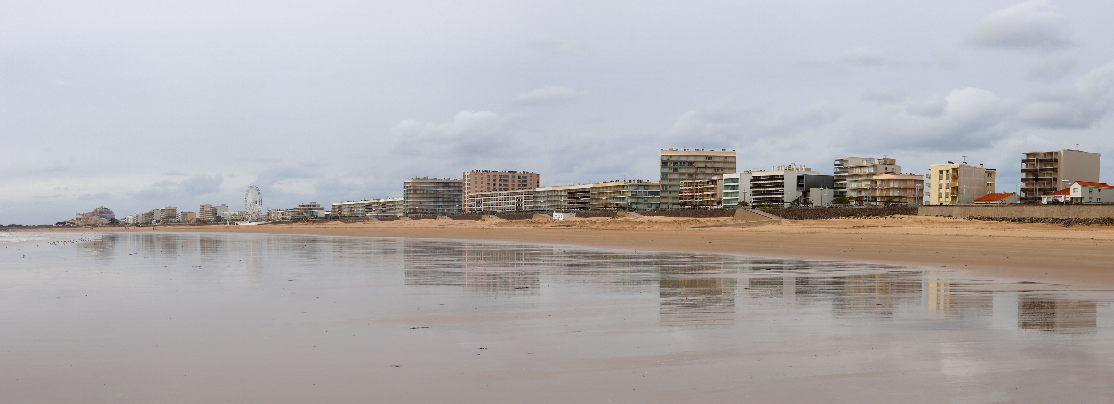 A beach with a sandy shore and a row of buildings in the background.