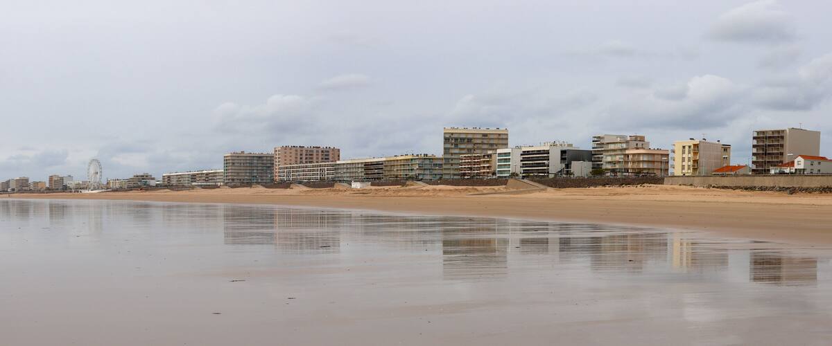 A beach with a sandy shore and a row of buildings in the background.