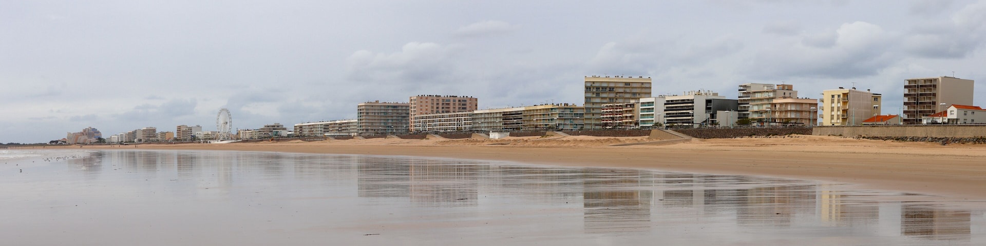 A beach with a sandy shore and a row of buildings in the background.