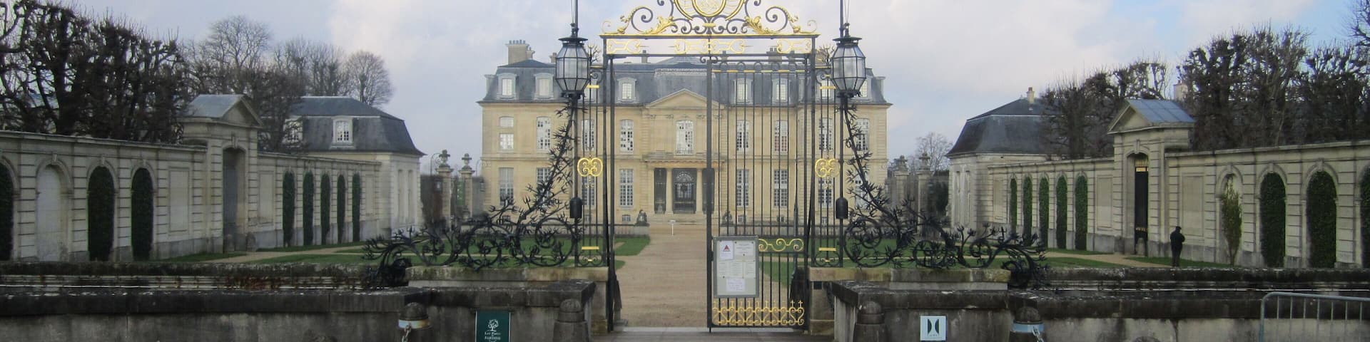 A grand entrance with a golden gate, a cobblestone pathway, and classical architecture.