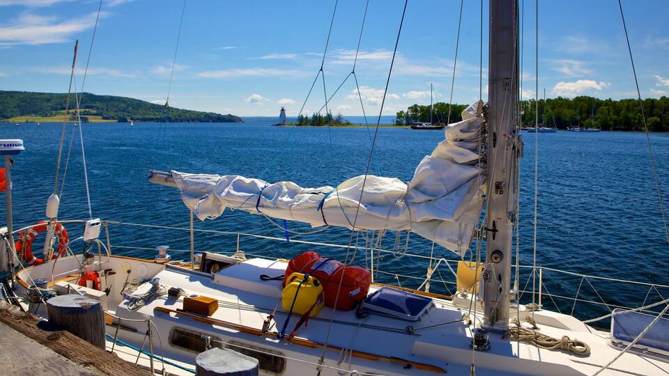 A sailboat docked near a lighthouse, with a forested island in the background and calm waters.