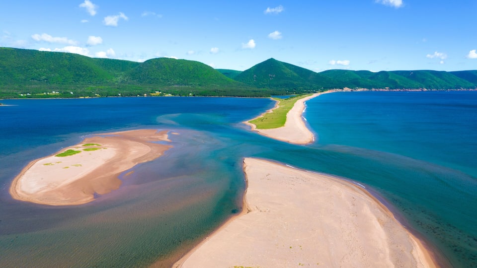 A coastal landscape with a sandy beach, clear blue waters, and green hills in the background.