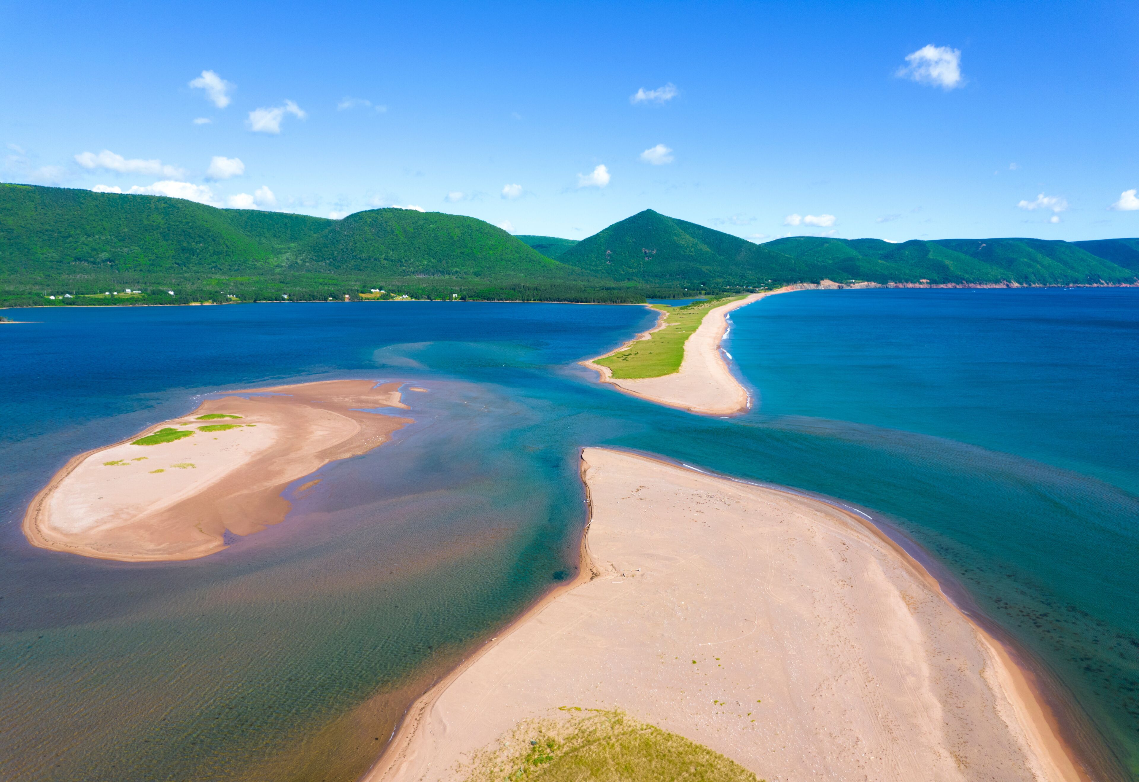 A coastal landscape with a sandy beach, clear blue waters, and green hills in the background.