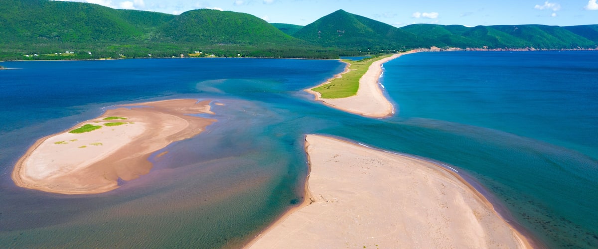 A coastal landscape with a sandy beach, clear blue waters, and green hills in the background.