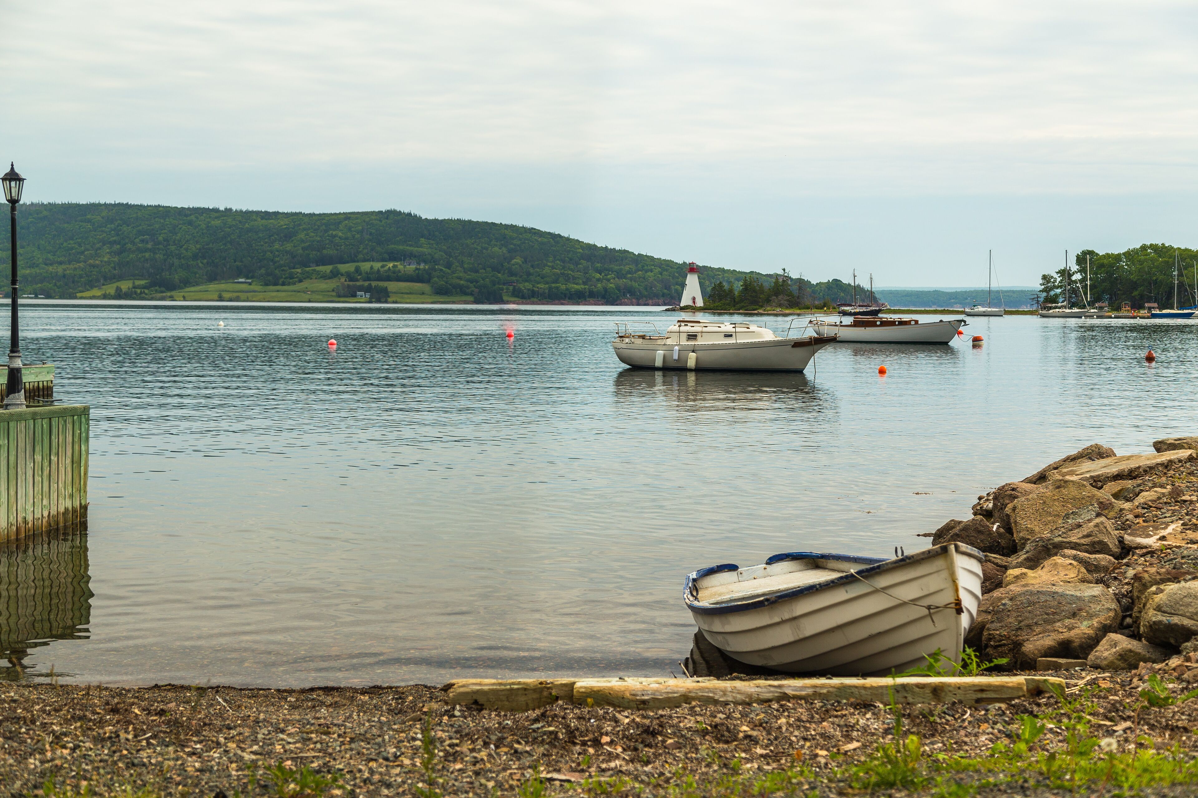 A calm lake with boats, a lighthouse, and a rocky shoreline.