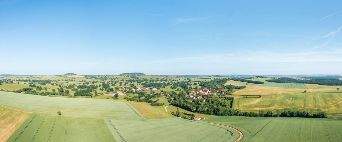 A rural landscape with rolling hills, fields, and scattered houses.