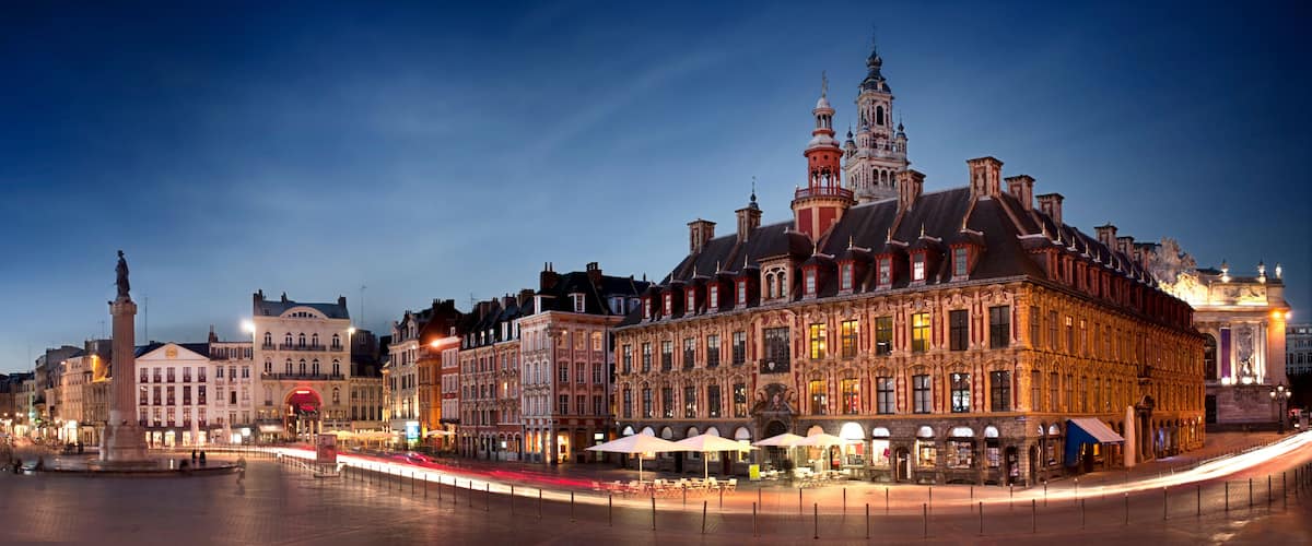 A historic European city square at dusk with illuminated buildings and a prominent clock tower.
