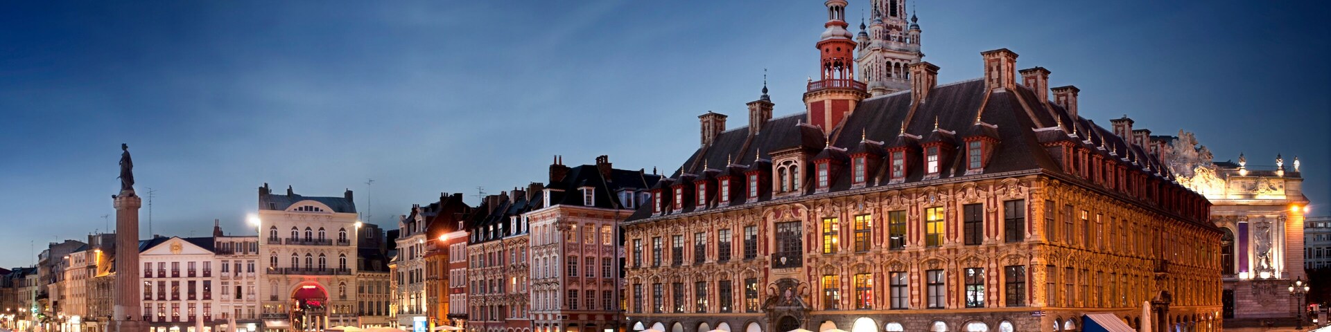 A historic European city square at dusk with illuminated buildings and a prominent clock tower.