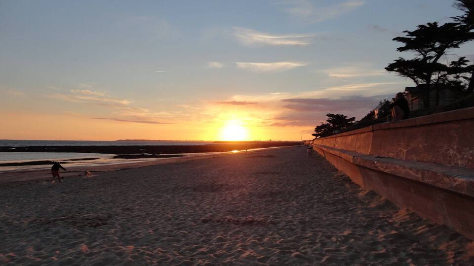 A beach at sunset with a clear sky, a low sun, and a distant shoreline.
