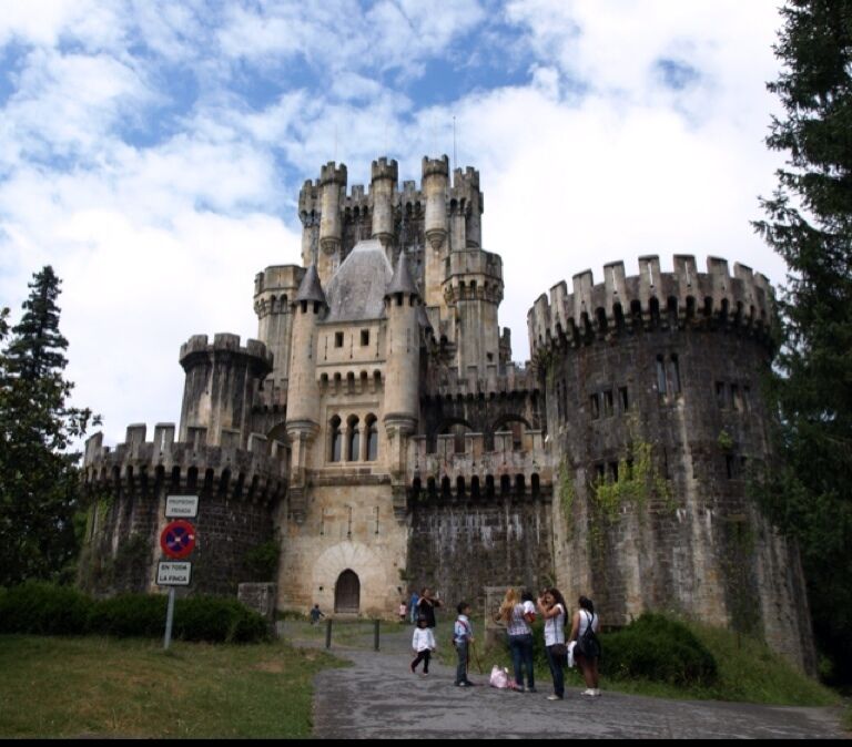 A historic castle with multiple towers, a large arched entrance, and a sign indicating a no parking zone.